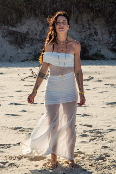 Woman in a white dress standing on a sandy beach with a natural background