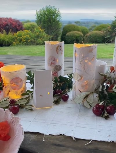 Decorative candles with floral designs on a white surface with a garden view in the background.