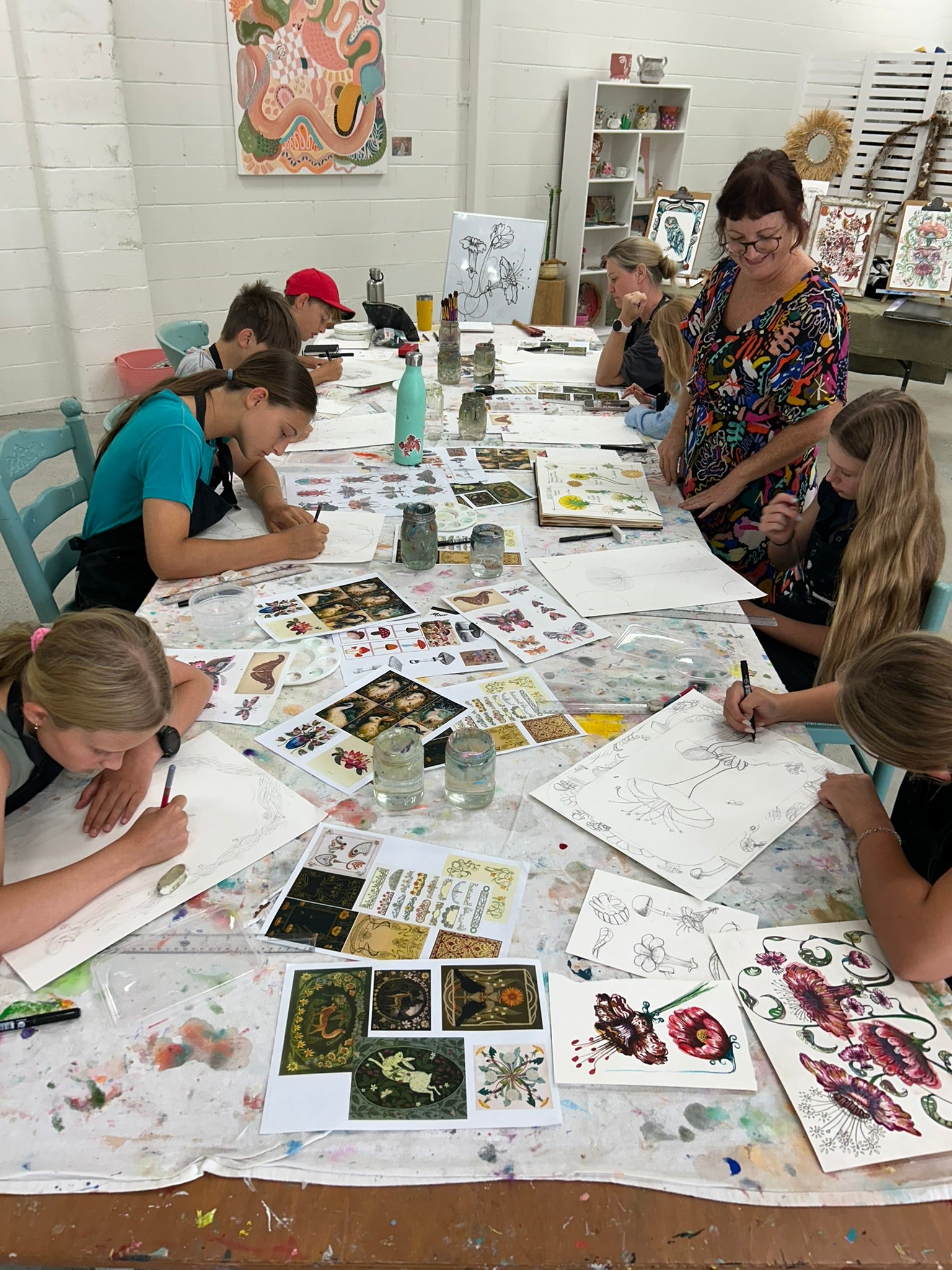 Group of people working on art projects at a table with various materials and artworks.