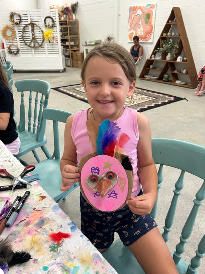 Child holding a decorated paper plate in a room with art supplies and furniture.