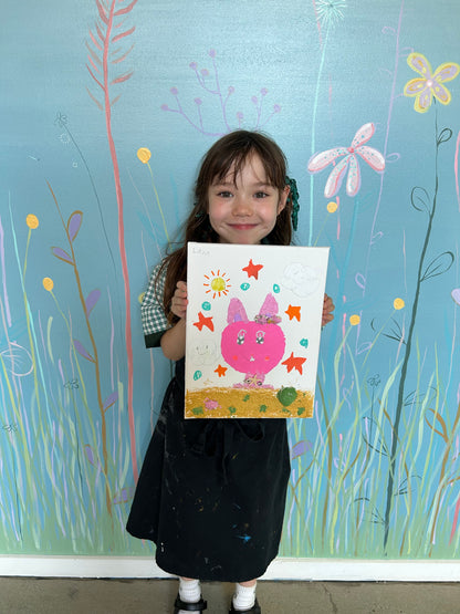 Child holding a drawing of a pink character with a blue background