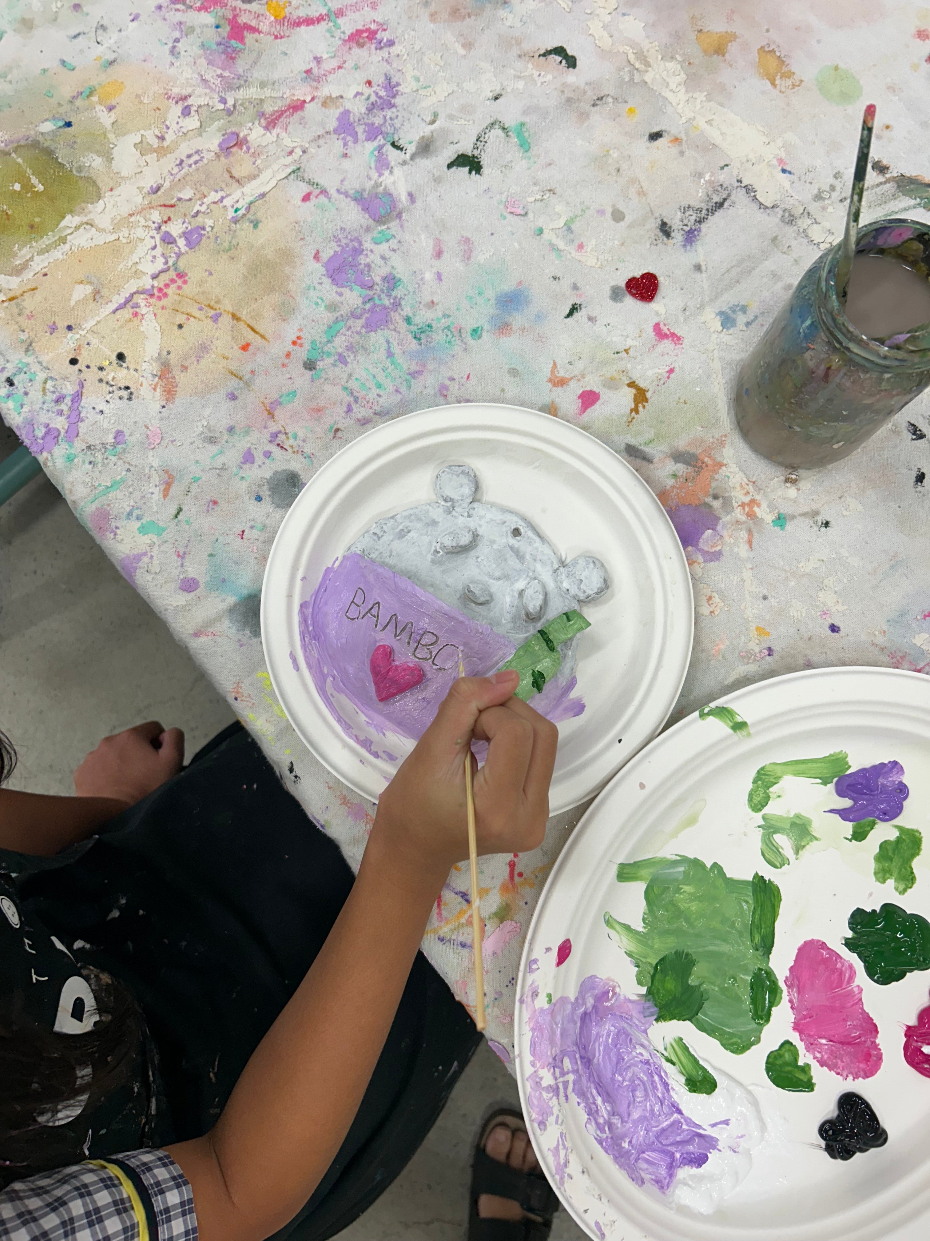 Person painting on a paper plate with various colors and a paintbrush.