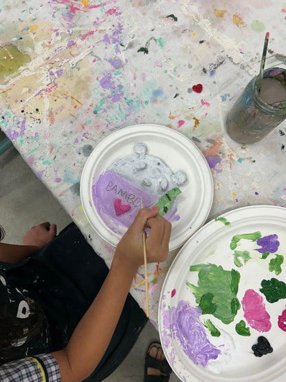 Person painting on a paper plate with various colors and a paintbrush.