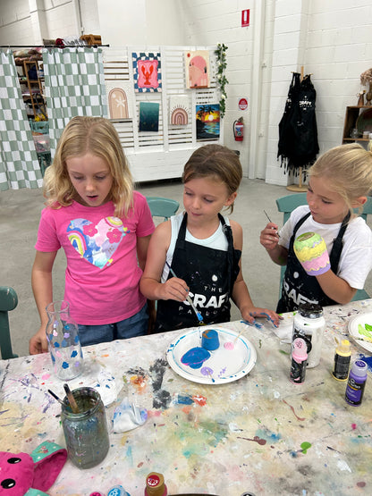 Three children engaged in an art project at a table with various art supplies.