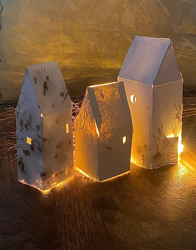Three wooden house-shaped lanterns with a warm glow on a textured surface.